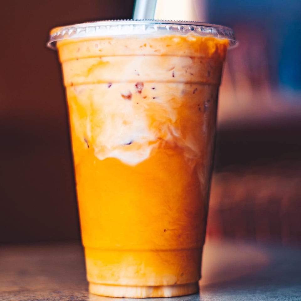 A vibrant orange and white layered Thai iced tea in a clear plastic cup with a lid.