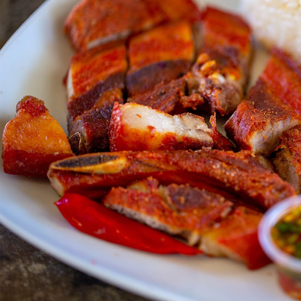 Crispy Hmong pork belly with red chilies and dipping sauce on a white plate.