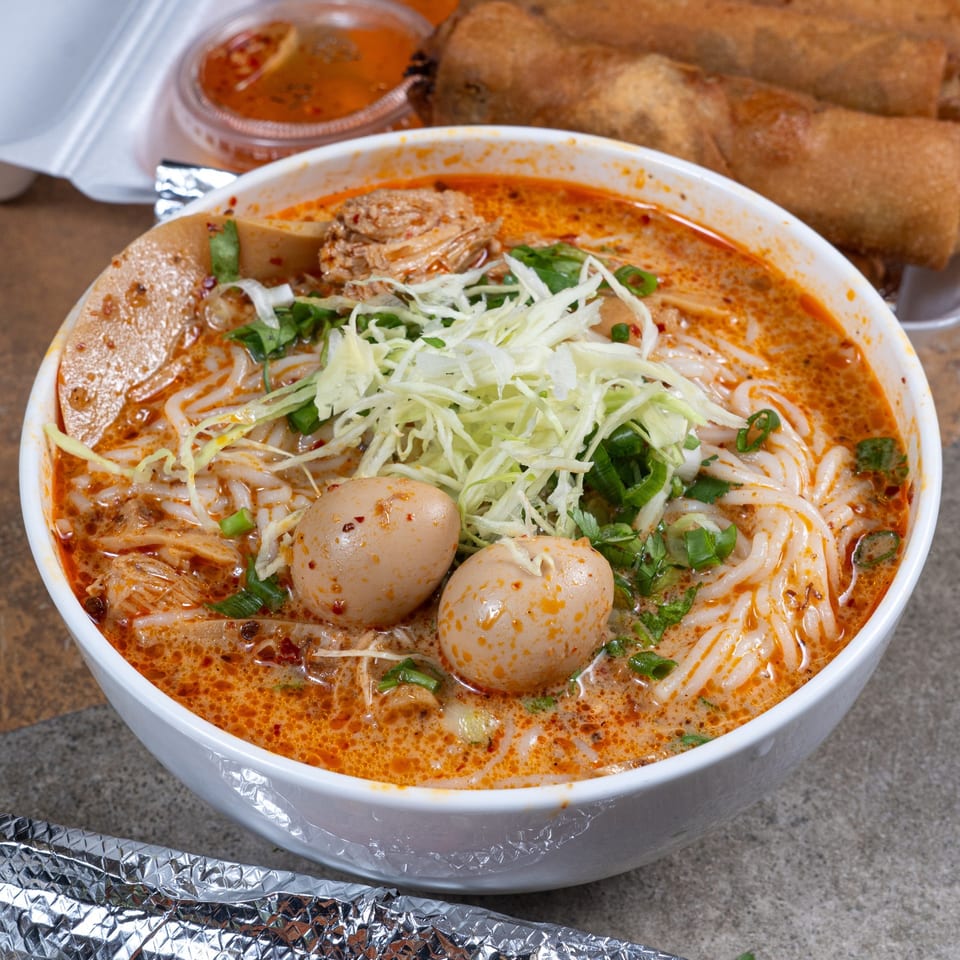 A bowl of Malee's Kitchen Hmong noodle soup with two eggs, shredded cabbage, and green onions.
