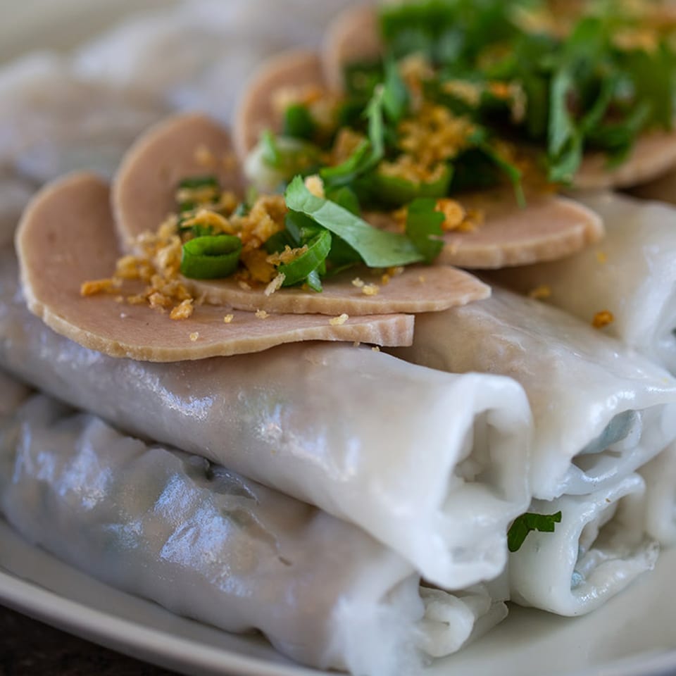Hmong steamed rice rolls topped with sliced pork sausage, crispy garlic, and fresh herbs.